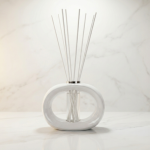Gloss white porcelain reed diffuser with white sticks on marble surface, minimalist home décor
