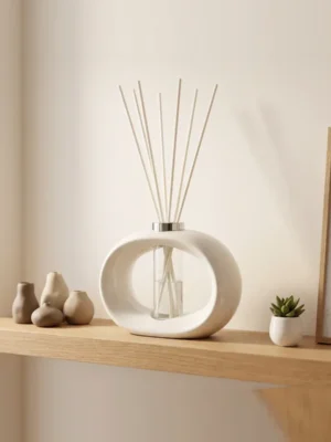 White porcelain Amberly reed diffuser with 45cm fibre reeds styled on an oak floating shelf in a modern living room